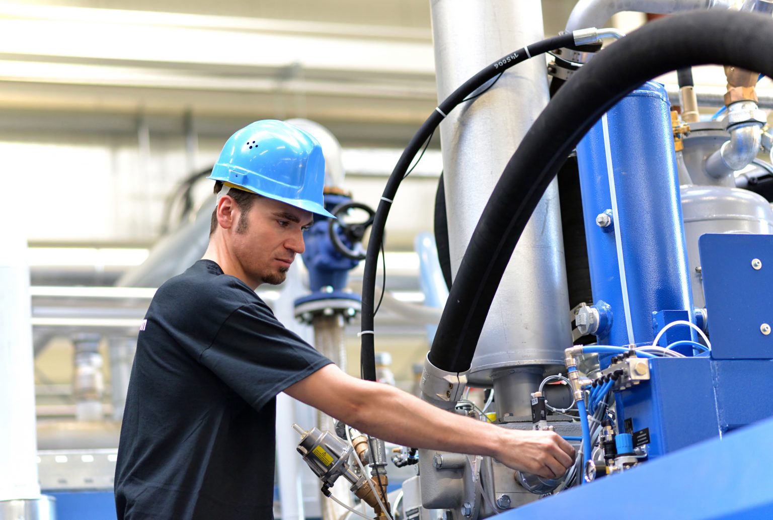 Katzinger Servicetechniker mit Helm nimmt Industrianlage mit großen Hydraulikschläuchen in Betrieb.